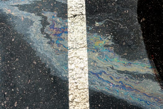 Oil spill on wet asphalt, parking lot with dividing line.
