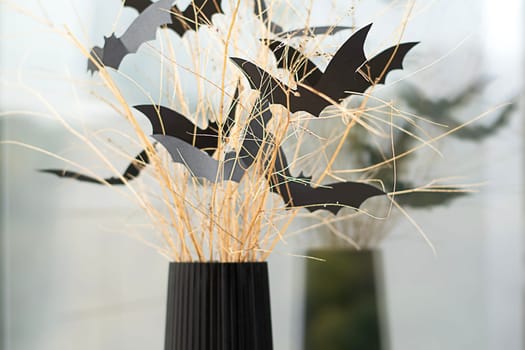 Halloween. Concept. Autumn holiday. Scary bats made of black paper, on dry branches in a black vase. Against the background of the window. Reflection. Background. Close-up. Soft focus.