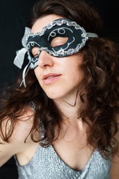 Portrait of a mysterious attractive woman in a carnival mask. Black background, lace mask on the face, shiny dress. Halloween party and parade concept