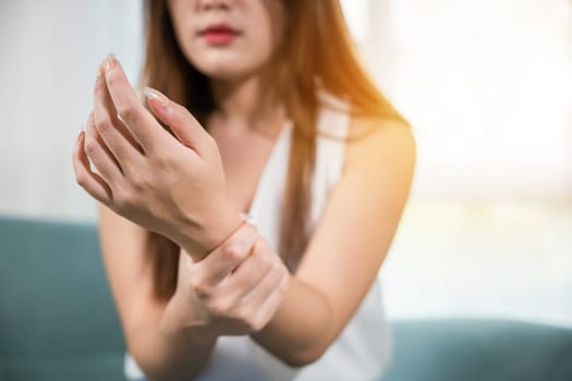 Closeup hand. Asian woman hand problem injury feeling joint pain, young female sitting on sofa holds suffering her wrist at home, performing self-massage, Health care and medical concept