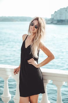 a woman in a black dress stands at the railing near the sea walk