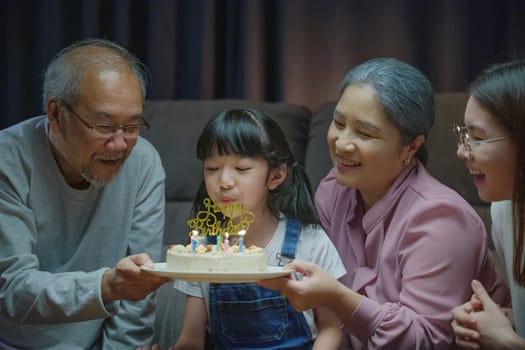 Birthday surprise. Happy Asian family grandparents and mother celebrating enjoy birthday party with cake of granddaughter at home in night time