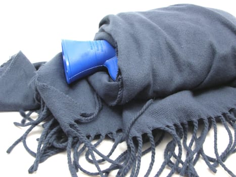 Blue hot water bottle wrapped in blue scarf with fringe