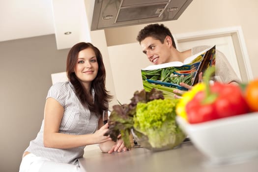 Young couple in kitchen choosing recipe from cookbook