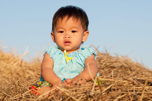 Baby girl from Asia sits on straw