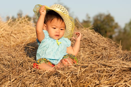 Baby girl from Asia sits on straw