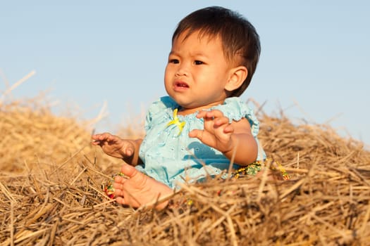 Baby girl from Asia sits on straw