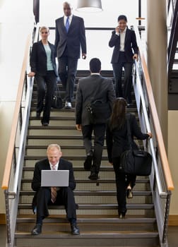 Businessman sitting on busy stairs with laptop. Vertically framed shot.