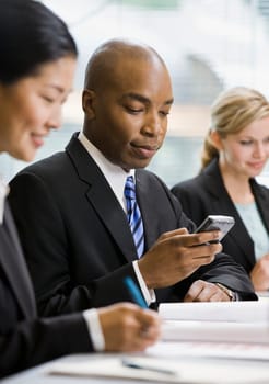 Businessman sitting at conference table texting. Vertically framed shot.