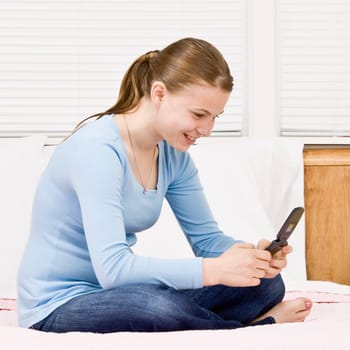 Young girl sitting on bed texting. Square framed shot.