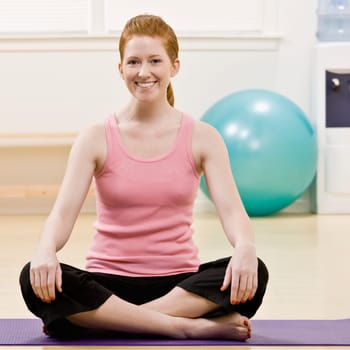 Young woman sitting cross legged on mat. Square format.