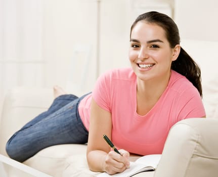 Young woman lying on couch and writing in journal. Horizontally framed shot.