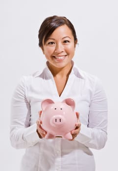 A beautiful and young asian woman holding a piggy bank. She is smiling at the camera. Vertically framed shot.