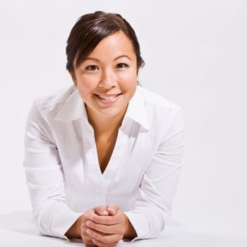 A young woman wearing white is in an isolated white room and is smiling at the camera. Square framed shot.