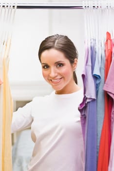 A beautiful brunette looking through clothing in a closet. She is smiling at the camera. Vertically framed shot.