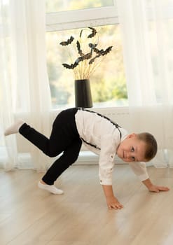 Halloween concept. Autumn holiday. A boy dances against the background of a window near a black vase with bats cut out of paper on dry branches. Close-up. Background.