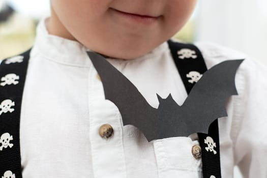 Halloween concept. Autumn holiday. Little boy, no face. In the pocket of a white shirt sits a bat made of black paper. Portrait. Close-up. Soft focus. Background.