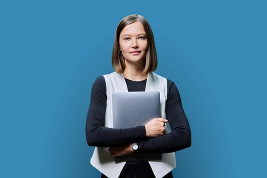 Serious young business woman with laptop on blue studio background. Successful confident caucasian female looking at the camera. Business, work, job, study, education, e-learning, technology concept