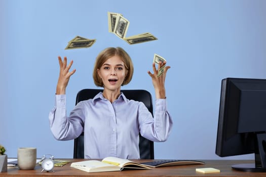 successful businesswoman throwing money while sitting on chair at desk. banknotes fly in the air
