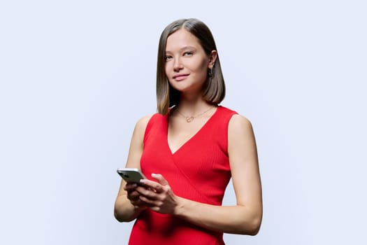 Young fashionable modern woman holding smartphone in hands, looking at camera on white studio background. Technology, mobile applications, work leisure education lifestyle communication, youth people