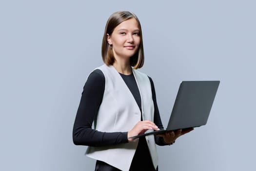 Smiling young business woman with laptop on grey studio background. Successful confident caucasian female looking at camera. Business, work, job, study, education, e-learning, technology concept