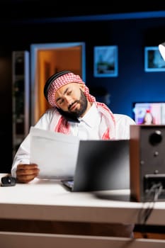Detailed shot of Arab man using a laptop and mobile device for communication and research, showcasing proficiency in technology. Muslim guy multitasking, talking on his cellphone and comparing notes.