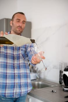 Details on the hands holding bottle of white wine and pouring it into a wine glass. Young adult Caucasian man opening a red wine bottle at home in the minimalist home kitchen interior