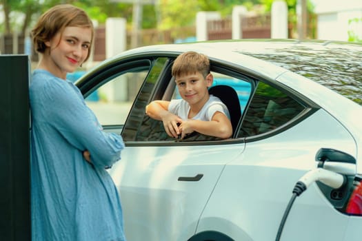 Environmental awareness family with eco-friendly electric car recharging battery from home EV charging station with little boy inside the car. Rechargeable and EV car technology. Perpetual