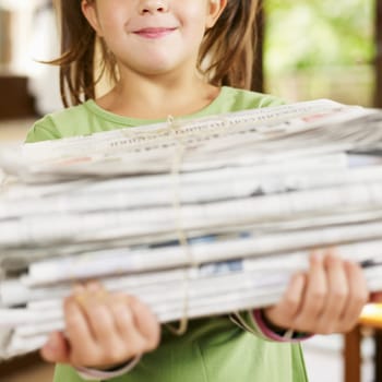 girl carrying newspapers for recycling, looking at camera