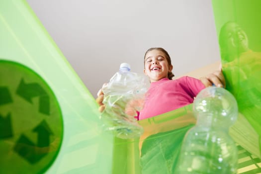 Girl holding plastic bottles for recycling, viewed from inside recycling bin. Copy space