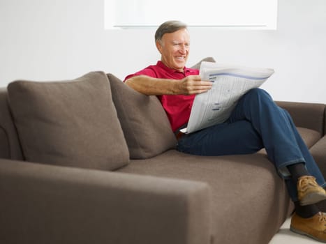 senior man reading newspaper at home and smiling