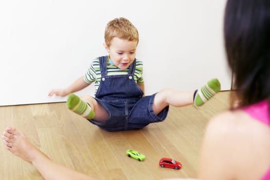 mother and son sitting on floor and playing with toy cars.