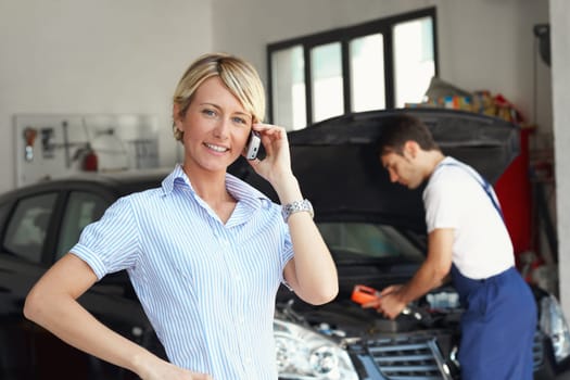 portrait of female client talking on mobile phone in auto repair shop.