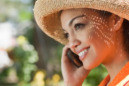 Close-up side view of a smiling young woman using a cell phone in an outdoor setting. Horizontal format.