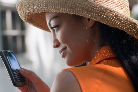 Close-up side view of a young woman wearing a sun hat and texting on her cell phone. Horizontal format.
