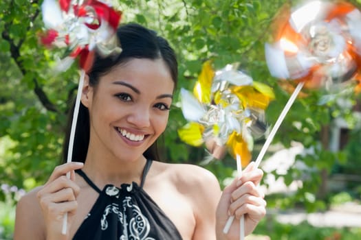 Close-up of a happy young woman outdoors, holding three pinwheels.  Horizontal format.