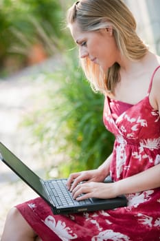 Profile of a young woman using a laptop outdoors. Vertical format.