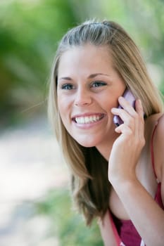 Close-up of a smiling young woman using a cell phone in an outdoor setting. Vertical format.