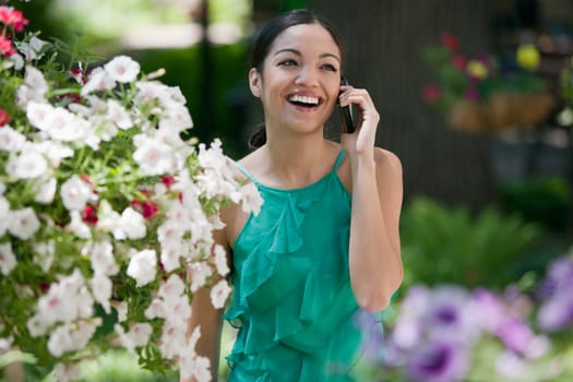 A young woman smiles while talking on her cell phone in a garden. Horizontal format.