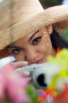 Close-up of a young woman in a sun hat, taking pictures of flowers. Vertical format.