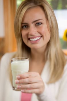 A young woman is holding a glass of milk and smiling at the camera.  Vertically framed shot.