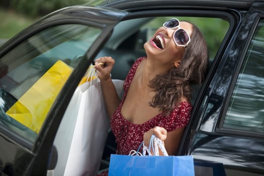 Young woman getting out of car holding shopping bags. Horizontally framed shot.