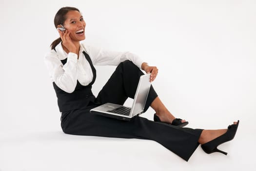 Young woman sitting on floor using laptop and wearing bluetooth headset. Horizontally format.
