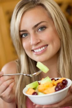 A young woman is holding a bowl of fruit and smiling at the camera.  Vertically framed shot.