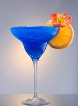 Blue Hawaiian mixed drink with orchid and orange garnish on plain background