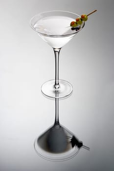 Martini mixed drink with olive garnish on a light grey background with reflection