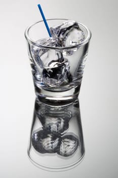 Empty mixed drink tumbler with ice on grey background with relfection