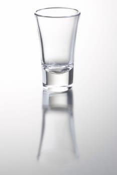 empty shot glass on grey background with reflection