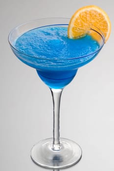 Frozen Blue Hawaiian mixed drink with orange slice garnish on grey background with reflection