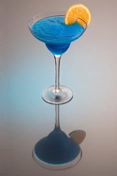 Frozen Blue Hawaiian mixed drink with orange slice garnish on grey background with reflection